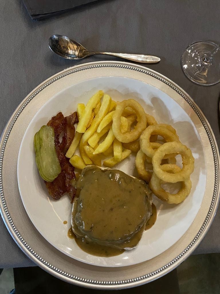 Plated steak with onion rings, fries and pickle on silver charger