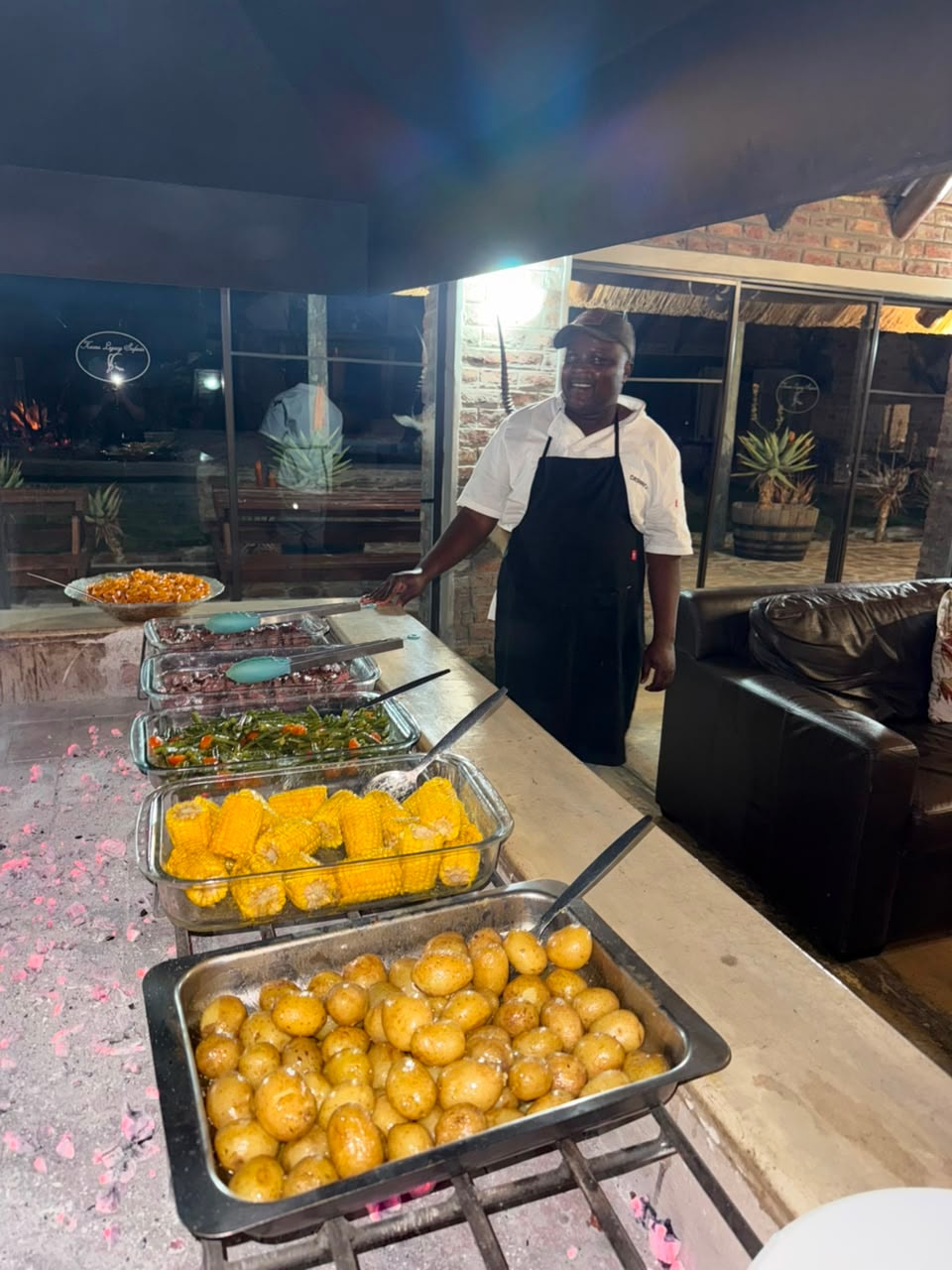 Chef smiling beside the outdoor boma buffet spread with corn, potatoes and steak