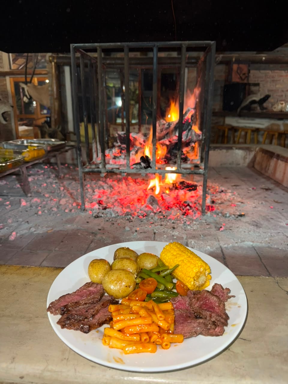 Grilled steak plate with baby potatoes, corn, green beans and pasta by the fire