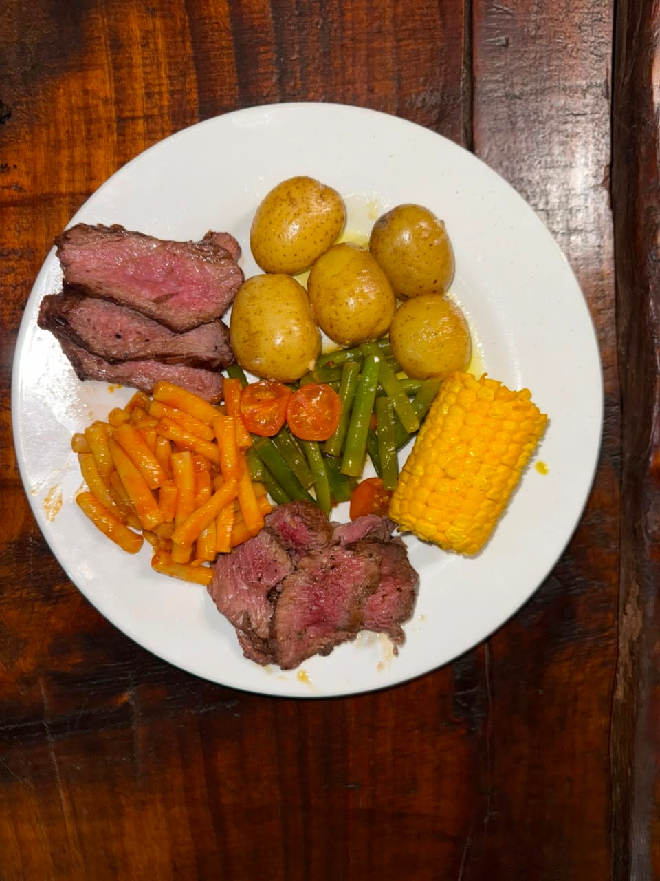 Overhead view of steak plate with baby potatoes, corn, green beans and pasta