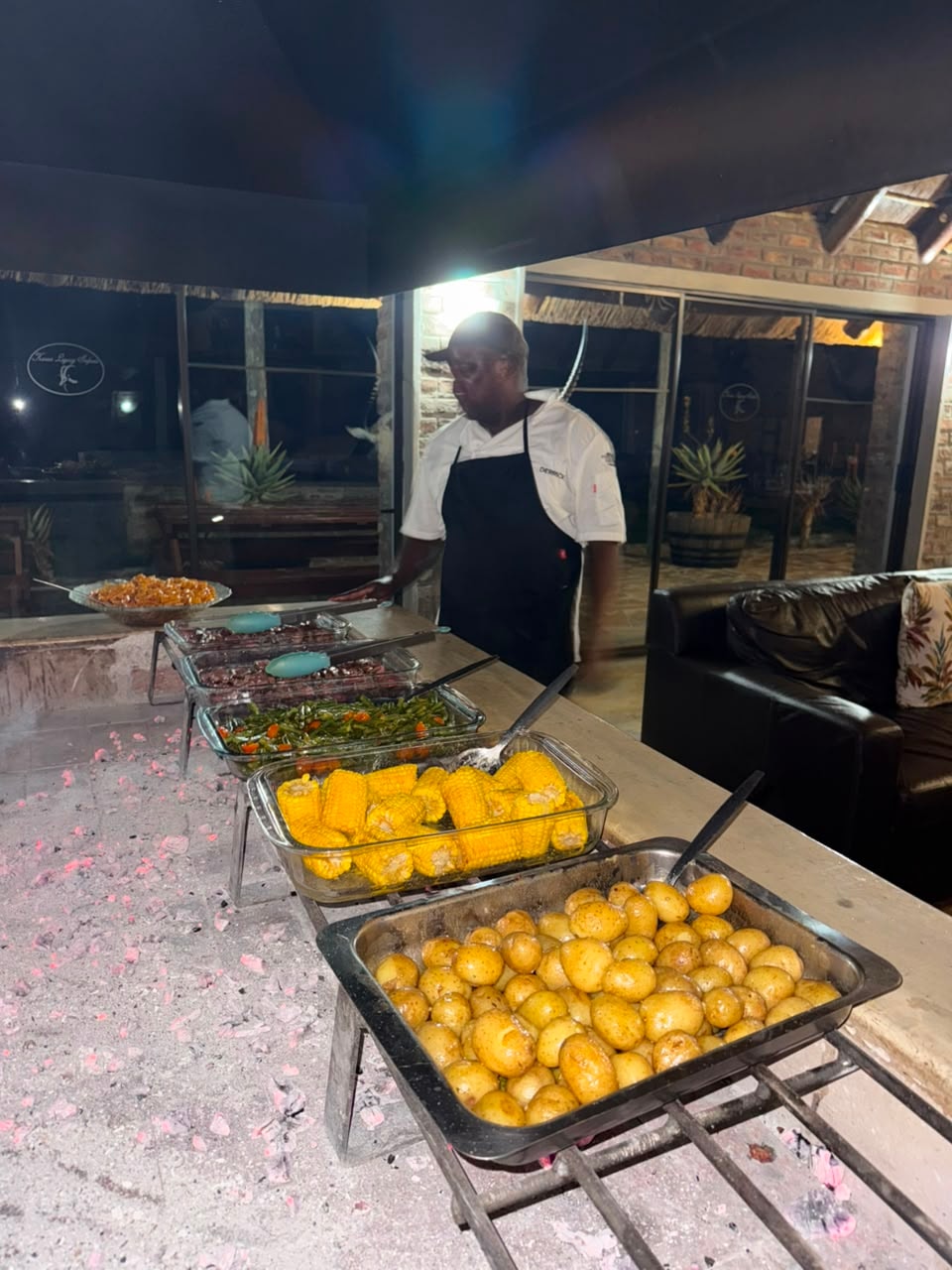 Chef standing beside the outdoor boma buffet with corn, potatoes and steak
